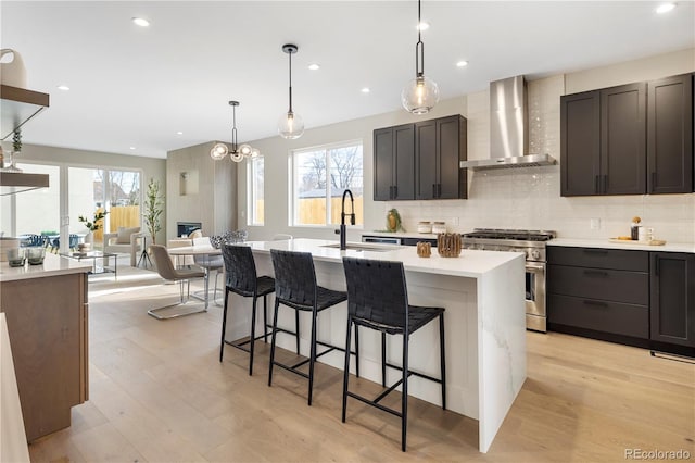 kitchen with sink, high end range, plenty of natural light, an island with sink, and wall chimney exhaust hood