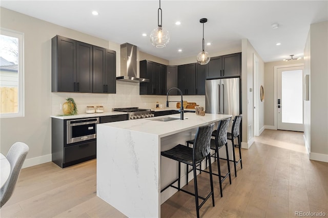 kitchen featuring appliances with stainless steel finishes, sink, a kitchen breakfast bar, light stone countertops, and wall chimney range hood