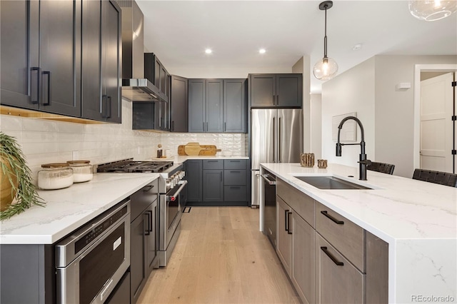 kitchen featuring pendant lighting, sink, high end appliances, light hardwood / wood-style floors, and wall chimney exhaust hood