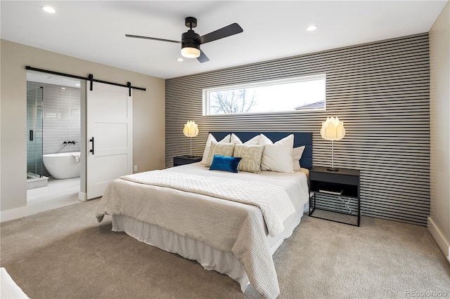 carpeted bedroom featuring a barn door, ceiling fan, and ensuite bathroom