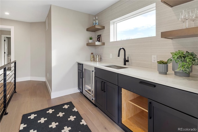 bar with tasteful backsplash, sink, light stone counters, and light wood-type flooring