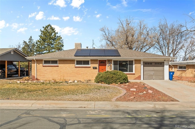 single story home with brick siding, solar panels, driveway, and a shingled roof