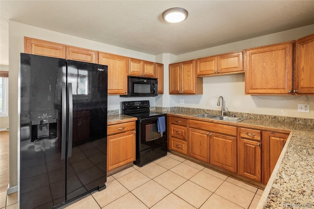 kitchen with black appliances, light tile patterned floors, brown cabinetry, and a sink