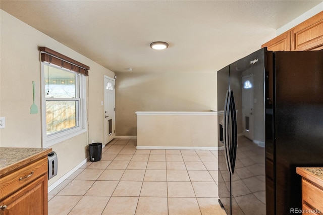 kitchen with light tile patterned floors, baseboards, black refrigerator with ice dispenser, and light countertops