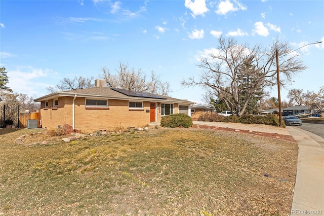 view of front of property featuring central air condition unit, a front lawn, roof mounted solar panels, fence, and brick siding