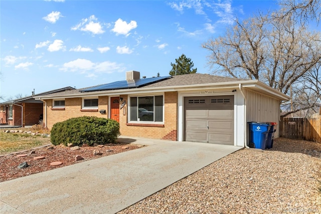 ranch-style house featuring driveway, fence, an attached garage, brick siding, and solar panels