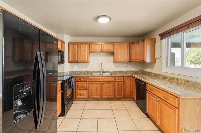 kitchen with light tile patterned flooring, brown cabinets, black appliances, and a sink