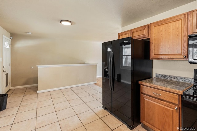 kitchen with dark countertops, light tile patterned floors, black appliances, and brown cabinetry