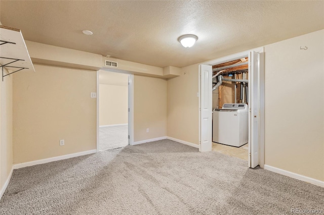 finished below grade area with light carpet, visible vents, washer / dryer, and a textured ceiling