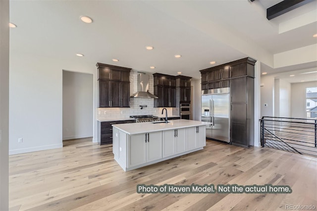 kitchen with sink, wall chimney exhaust hood, backsplash, an island with sink, and stainless steel built in fridge