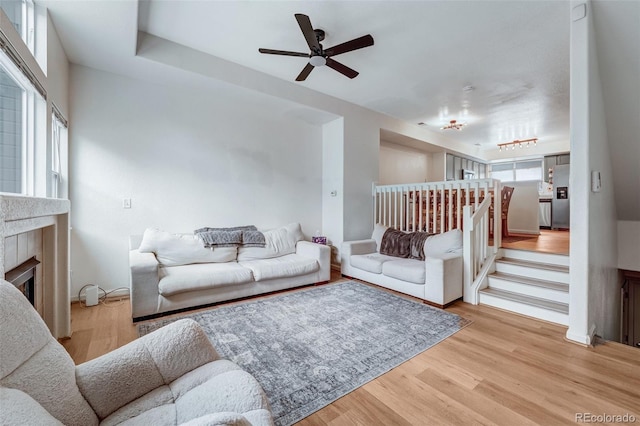 living area featuring a ceiling fan, light wood finished floors, and a fireplace