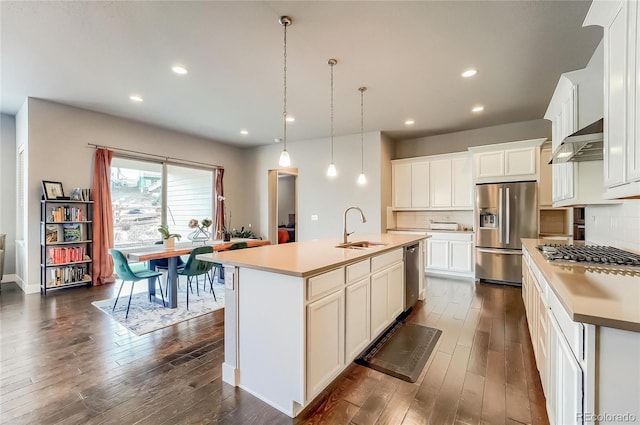 kitchen featuring appliances with stainless steel finishes, a sink, wall chimney range hood, and dark wood-style floors