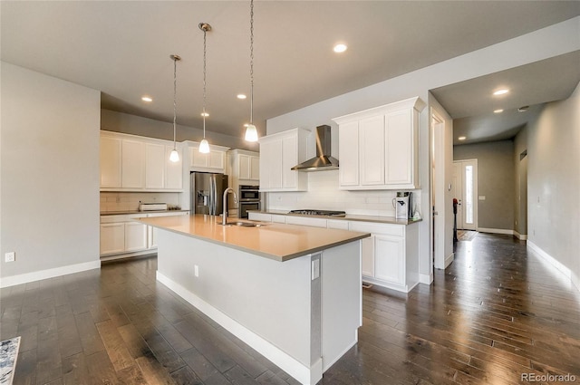 kitchen with dark wood-style floors, appliances with stainless steel finishes, a sink, an island with sink, and wall chimney exhaust hood