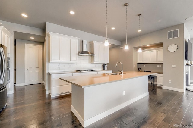 kitchen with dark wood-style flooring, a sink, visible vents, wall chimney exhaust hood, and an island with sink