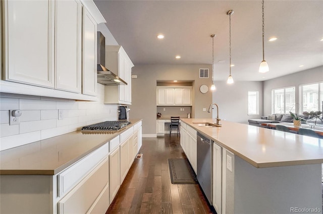 kitchen featuring stainless steel appliances, dark wood-type flooring, a sink, wall chimney range hood, and decorative backsplash