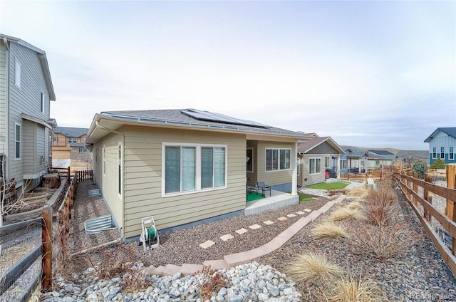 back of property with a fenced backyard, a residential view, solar panels, and a patio