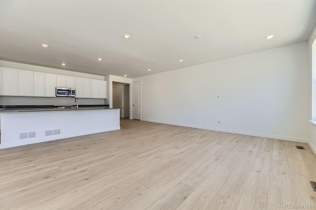 39867 Floyd St, Elizabeth, CO 80107 - kitchen featuring stainless steel microwave, dark countertops, white cabinets, light wood-style flooring, and recessed lighting
