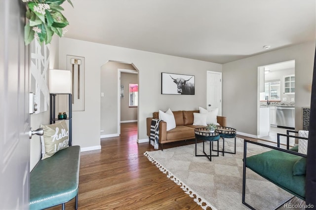 living room featuring arched walkways, baseboards, and wood finished floors