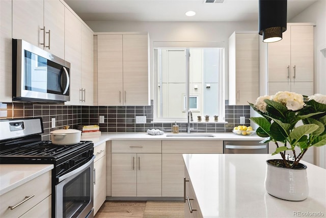 kitchen with light countertops, appliances with stainless steel finishes, decorative backsplash, and a sink