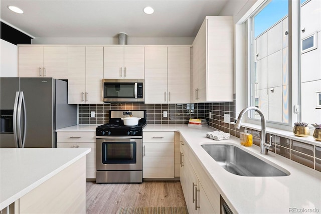 kitchen with a sink, light wood-style floors, backsplash, light countertops, and appliances with stainless steel finishes