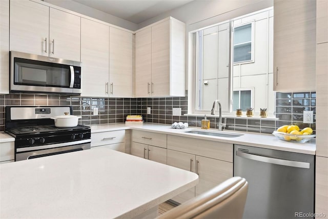 kitchen with a sink, modern cabinets, backsplash, light countertops, and appliances with stainless steel finishes