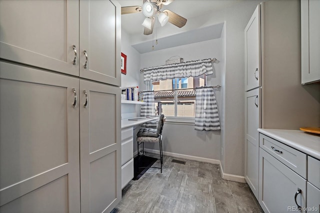 home office featuring built in desk, ceiling fan, and light hardwood / wood-style flooring