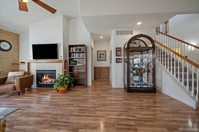 living room with hardwood / wood-style floors, high vaulted ceiling, a tile fireplace, and ceiling fan