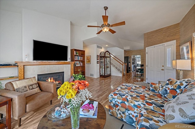 living room with a fireplace, high vaulted ceiling, ceiling fan, and light wood-type flooring