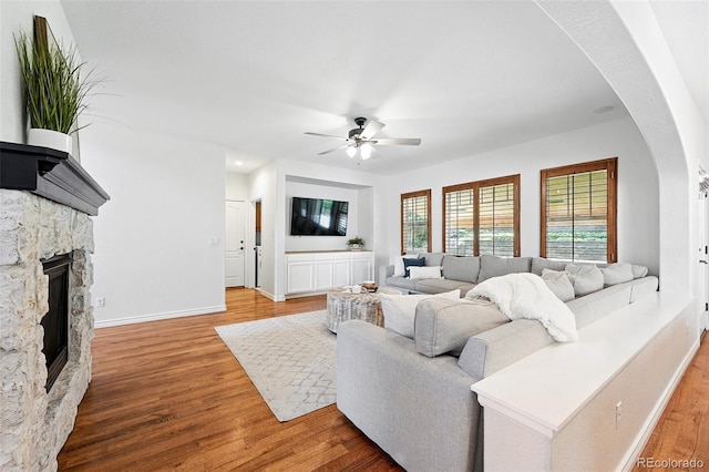 2832 Danbury Ave, Highlands Ranch, CO 80126 - living area featuring arched walkways, wood finished floors, a ceiling fan, a fireplace, and baseboards
