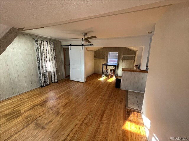 511 S Pennsylvania St, Denver, CO 80209 - unfurnished living room featuring a barn door, wood finished floors, wooden walls, and ceiling fan