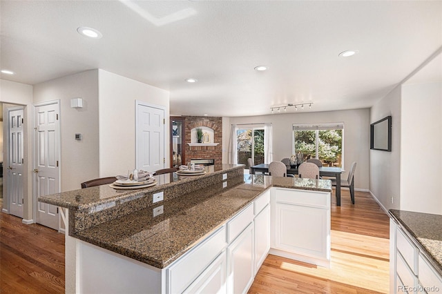 8825 Fairview Oaks Pl, Lone Tree, CO 80124 - kitchen featuring light wood-style flooring, a large fireplace, white cabinetry, recessed lighting, and dark stone counters