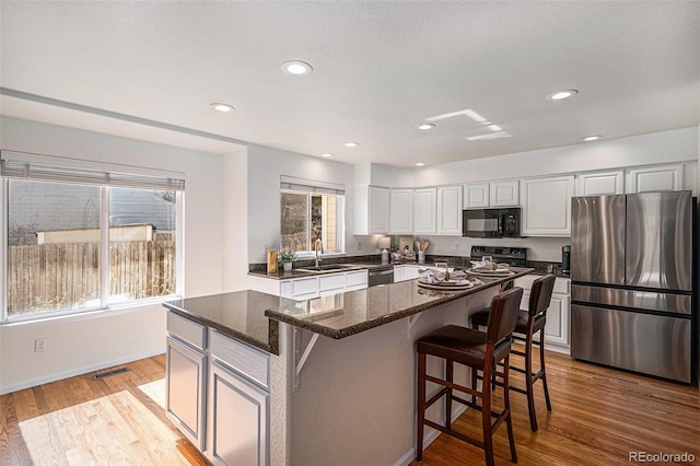 8825 Fairview Oaks Pl, Lone Tree, CO 80124 - kitchen featuring appliances with stainless steel finishes, white cabinetry, dark stone countertops, a kitchen bar, and a kitchen island