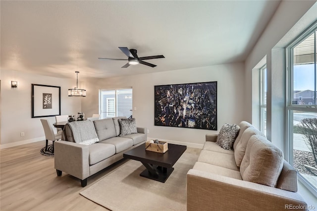 living room featuring ceiling fan with notable chandelier, plenty of natural light, light wood-style floors, and baseboards