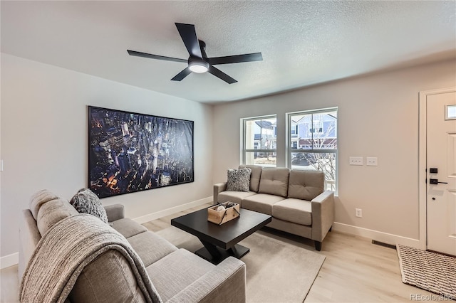 living room with light wood-type flooring, visible vents, a textured ceiling, baseboards, and ceiling fan