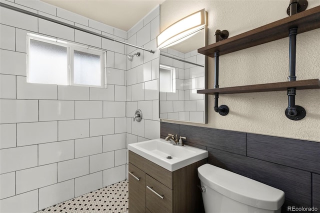 bathroom featuring tile walls, toilet, vanity, tiled shower, and a textured wall