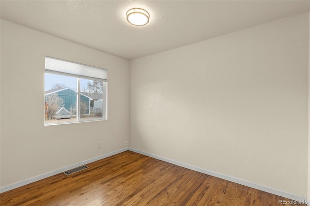 empty room featuring wood finished floors, a textured ceiling, baseboards, and visible vents