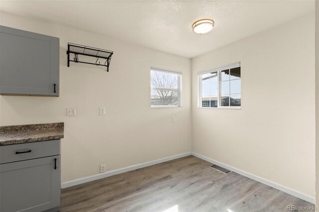 unfurnished dining area with light wood finished floors, baseboards, visible vents, and a textured ceiling