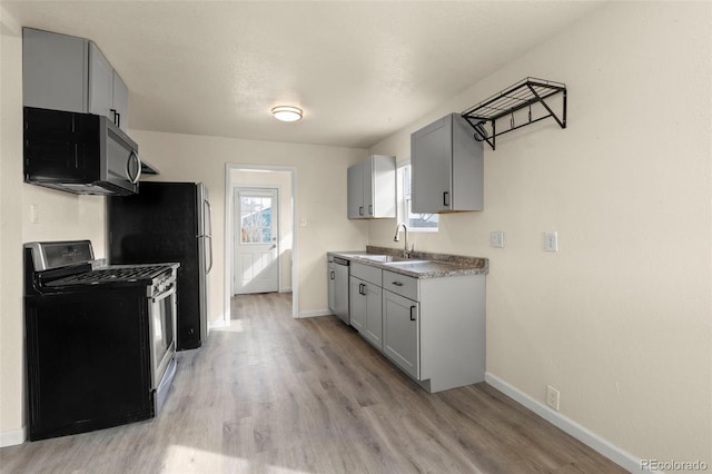 kitchen featuring baseboards, stainless steel appliances, a sink, light wood-style floors, and gray cabinetry