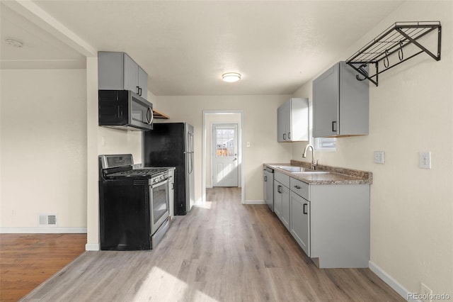 kitchen with a sink, appliances with stainless steel finishes, light wood-style floors, and baseboards