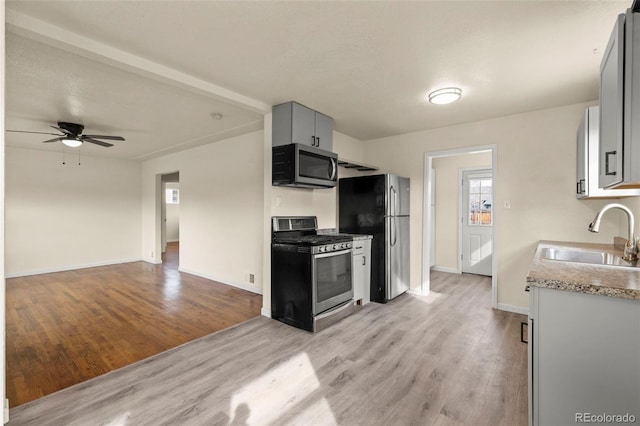 kitchen featuring light countertops, a sink, a ceiling fan, appliances with stainless steel finishes, and light wood-style flooring