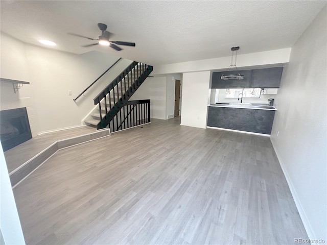 56 S Nome St, Aurora, CO 80012 - unfurnished living room featuring a fireplace with raised hearth, wood finished floors, stairway, ceiling fan, and a textured ceiling