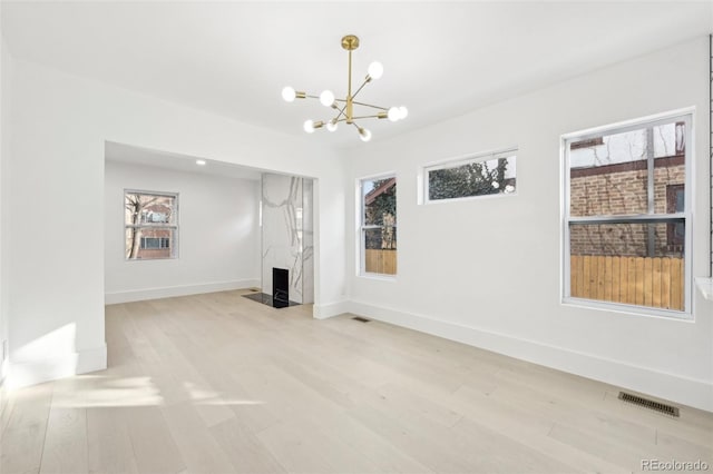 unfurnished living room with an inviting chandelier, a healthy amount of sunlight, light hardwood / wood-style floors, and a high end fireplace