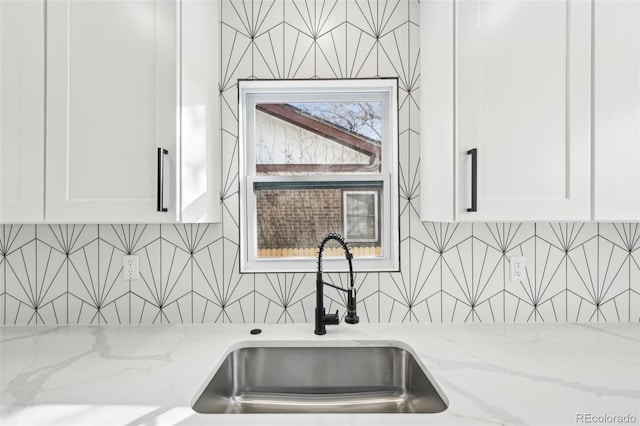 interior details with light stone counters, backsplash, sink, and white cabinets