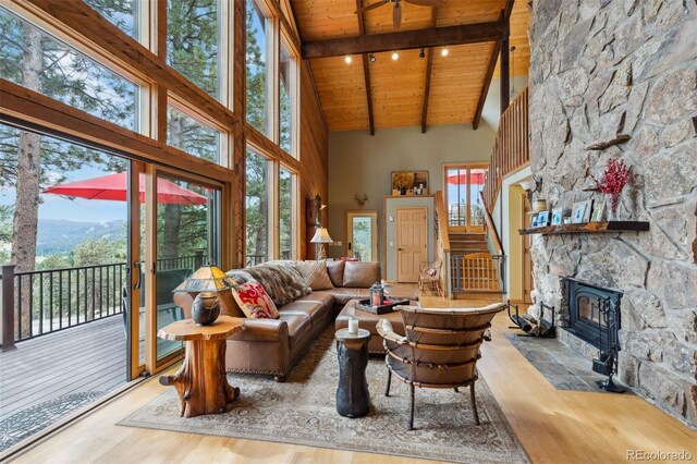 living room with high vaulted ceiling, a stone fireplace, wooden ceiling, light wood-type flooring, and beam ceiling