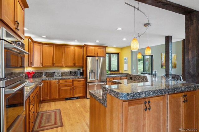 kitchen with pendant lighting, dark stone counters, a center island, light hardwood / wood-style flooring, and stainless steel appliances