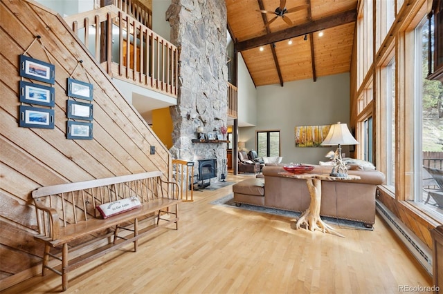 living room featuring high vaulted ceiling, a stone fireplace, wooden ceiling, ceiling fan, and a baseboard heating unit