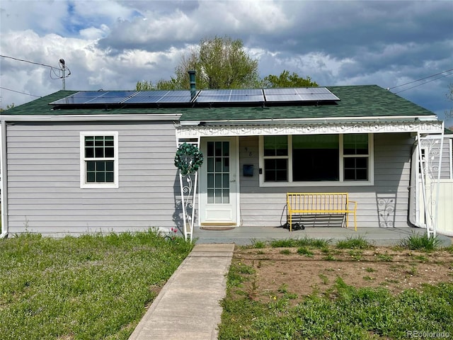 view of front facade featuring a shingled roof, covered porch, and roof mounted solar panels