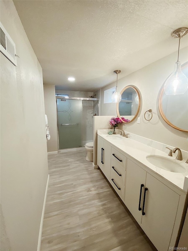 3000 Billings St, Aurora, CO 80011 - bathroom featuring wood finished floors, double vanity, toilet, a stall shower, and a textured ceiling