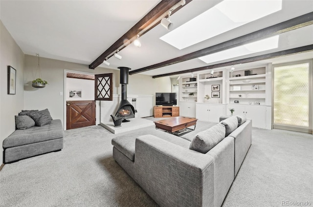 living room with a wood stove, a skylight, rail lighting, beamed ceiling, and light carpet