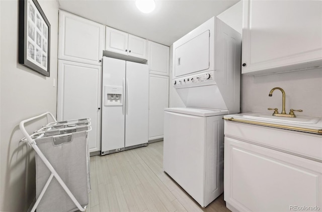 laundry room featuring cabinets, light wood-type flooring, sink, and stacked washer and clothes dryer